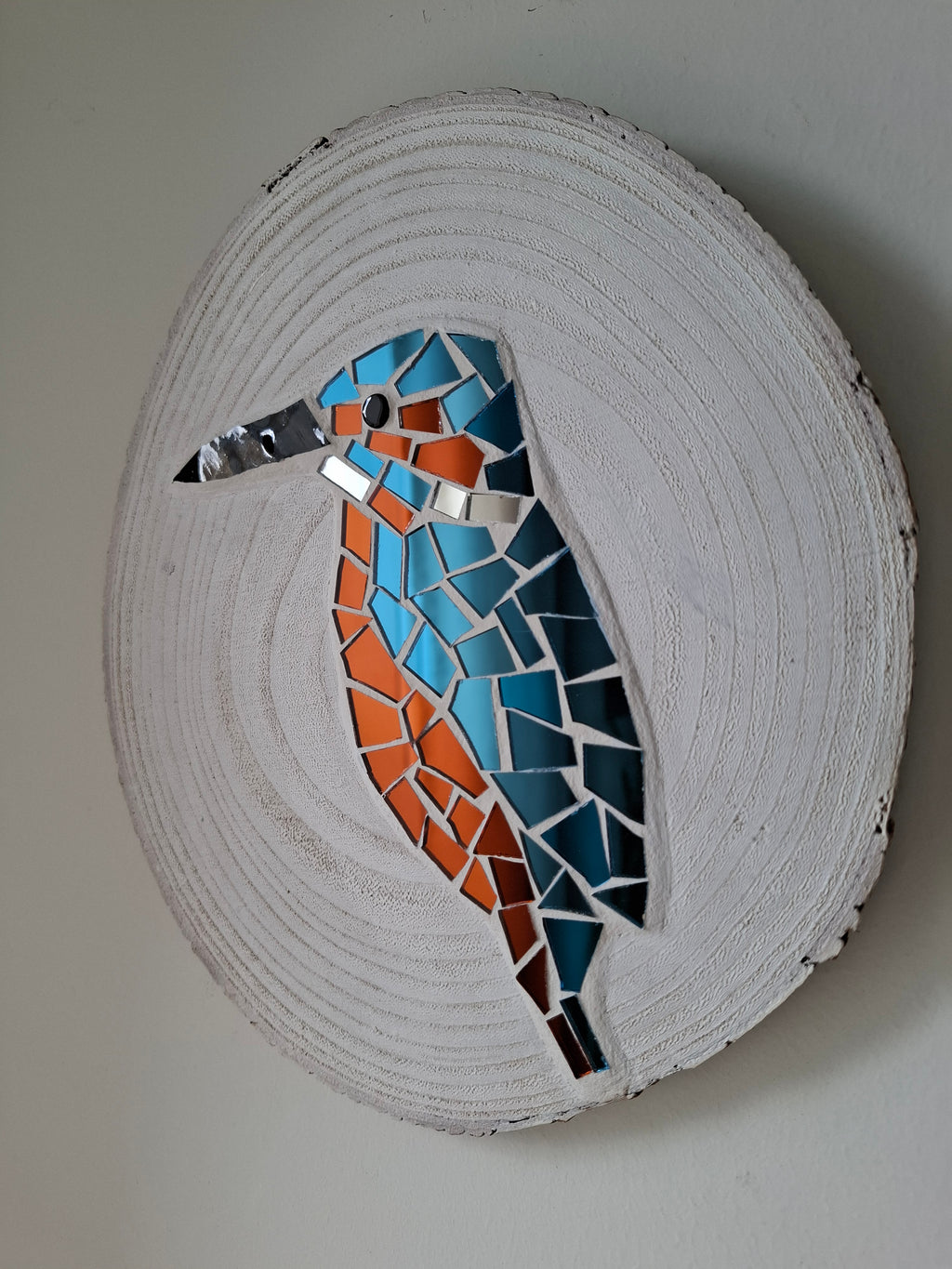 Side view of a circular kingfisher mosaic artwork, showing the rustic wood edge.
