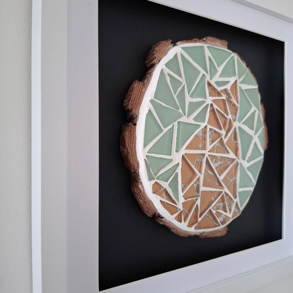 A framed circular mosaic wall art piece featuring a golden cat design in gold and mint green, mounted on a black backing inside a white frame.