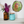 A round mosaic wall art piece featuring a colorful parrot on a green background, displayed on a white wall above a shelf with an amber glass vase of flowers and a blue glass jar.