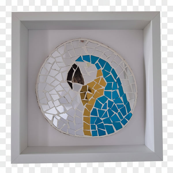 A circular mosaic wall art piece featuring a stylized parrot head in blue, gold, white, and black, mounted inside a square white shadow box frame.