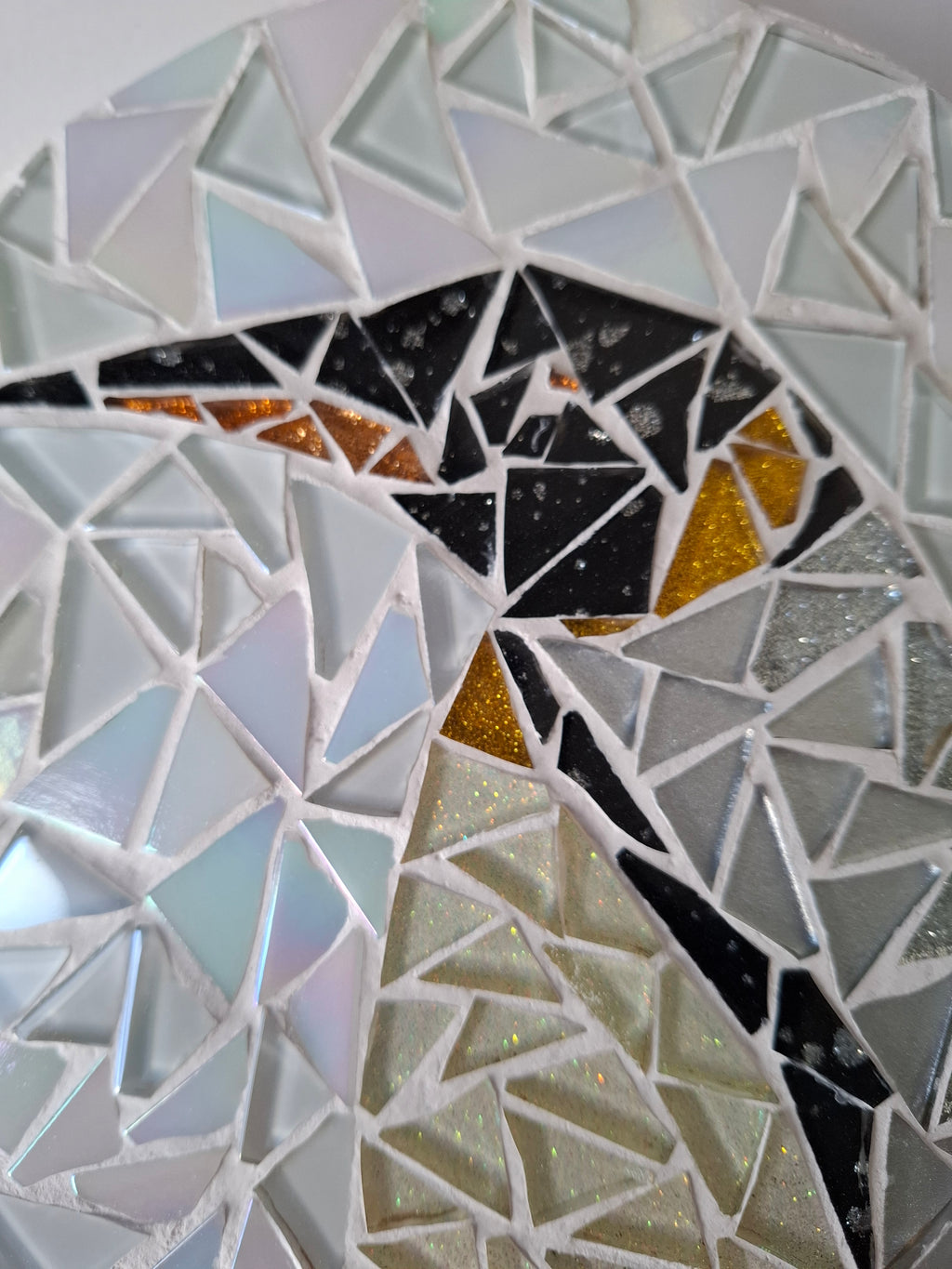 Side view of a circular penguin mosaic artwork, showing the rustic wood edge.
