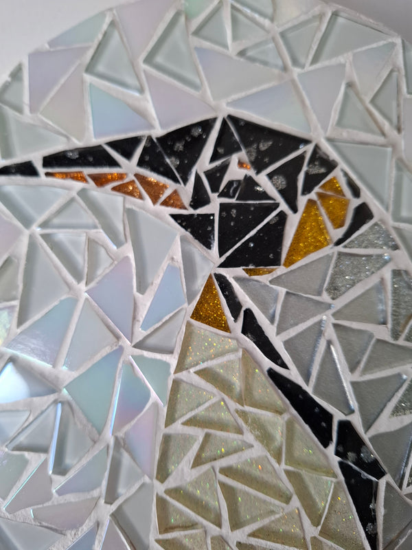 Side view of a circular penguin mosaic artwork, showing the rustic wood edge.