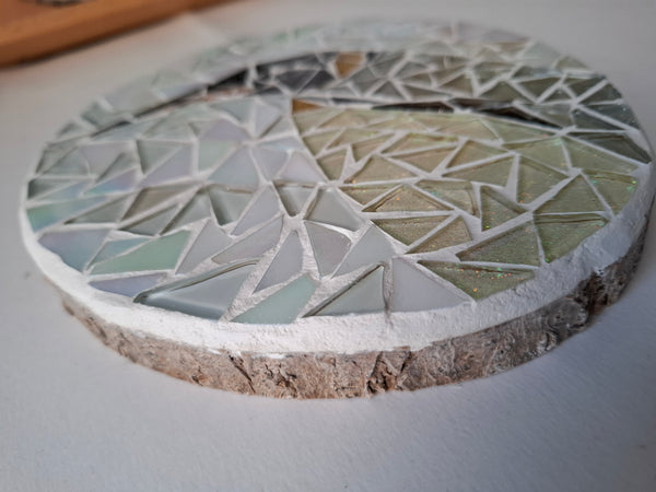 Side view of a circular penguin mosaic artwork, showing the rustic wood edge.