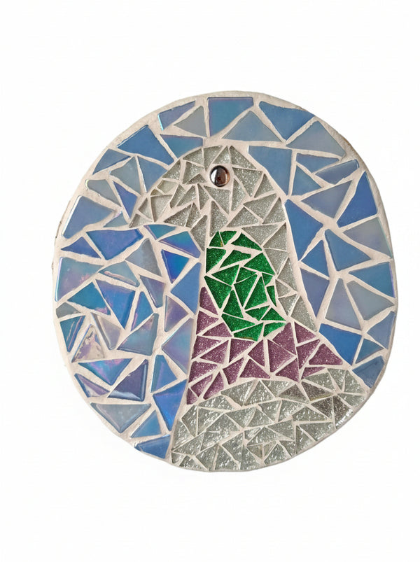 Circular mosaic wall art featuring a stylized pigeon design. Crafted with glittery silver, purple and green glass pieces on an iridescent blue background, set on rustic wood.