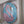 A circular mosaic wall art piece featuring a stylized flamingo design, made with blue, pink glitter, and silver mirror tiles, mounted inside a white frame. 