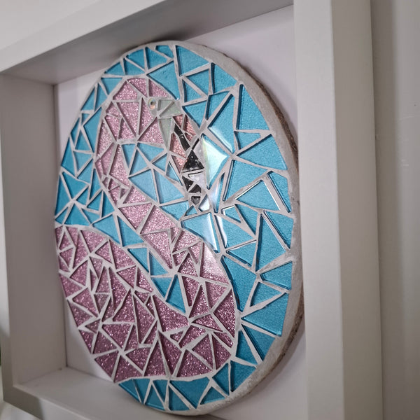 A circular mosaic wall art piece featuring a stylized flamingo design, made with blue, pink glitter, and silver mirror tiles, mounted inside a white frame. 