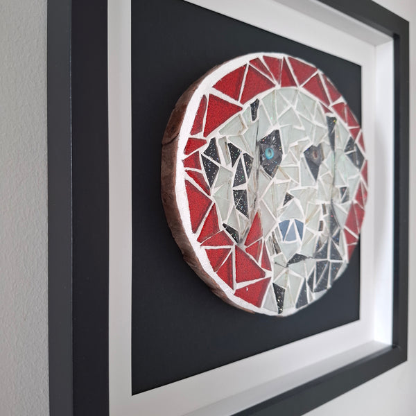 A circular mosaic wall art piece depicting a stylized dog, mounted inside a black frame with white matting on a light gray wall.