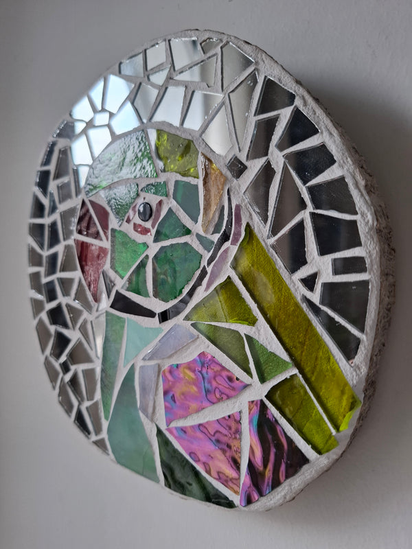 Side view of a circular parakeet mosaic artwork, showing the rustic wood edge.