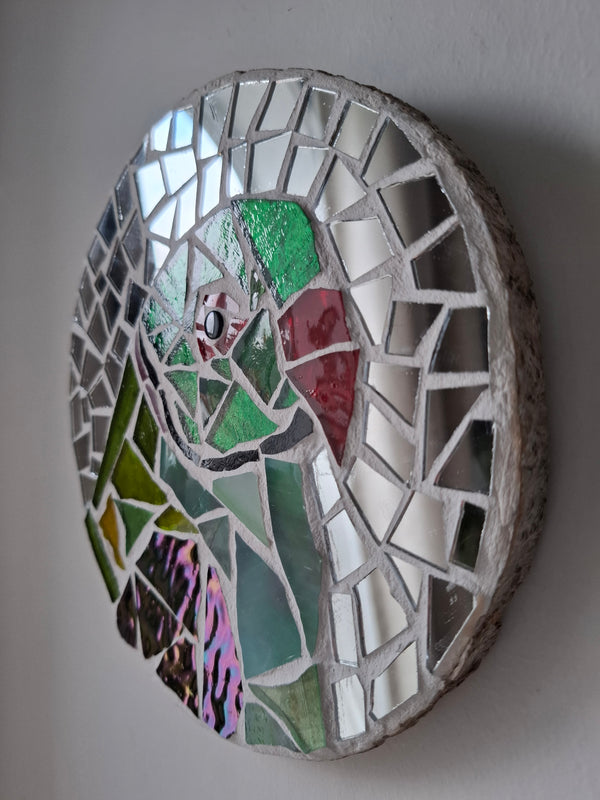 Side view of a circular parakeet mosaic artwork, showing the rustic wood edge.