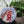 Circular mosaic wall art featuring a stylized robin design. Crafted with white, red, and brown glittery glass pieces on an iridescent blue background, set on rustic wood. Displayed on a table in a room with plants to show how beautiful the piece is in a home. 