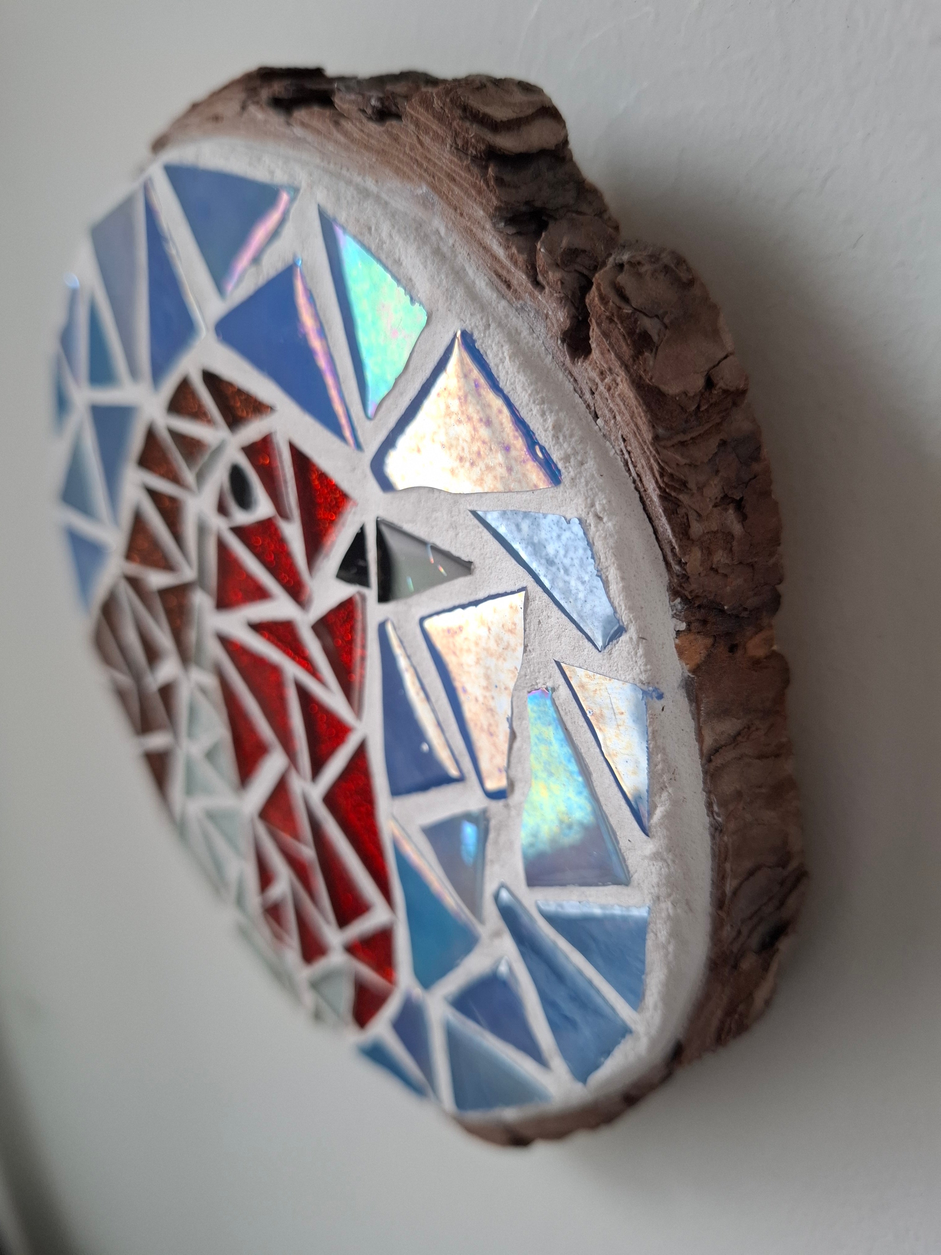 Side view of a circular robin mosaic artwork, showing the rustic wood edge.