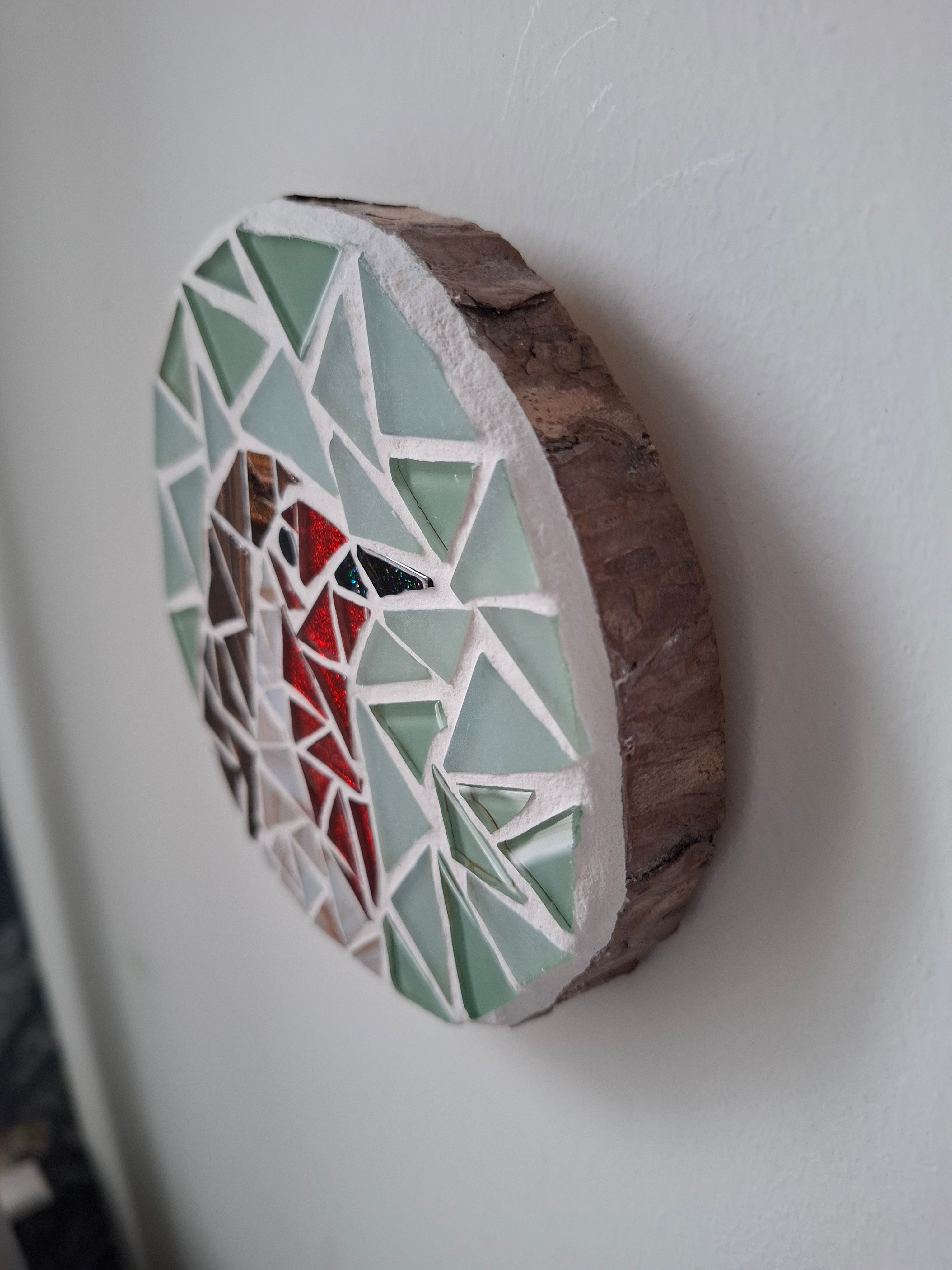 Side view of a circular mosaic robin artwork, showing the rustic wood edge.
