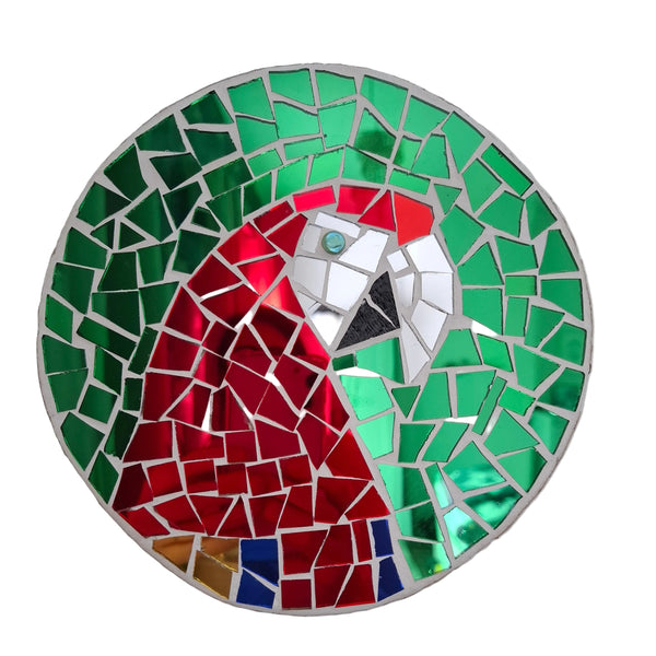 Circular mosaic wall art featuring a stylized macaw design. Crafted with reflective blue, red and gold mirror glass pieces on a reflective green mirror background, set on rustic wood.