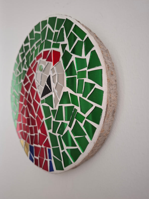 Side view of a circular macaw mosaic artwork, showing the rustic wood edge.

