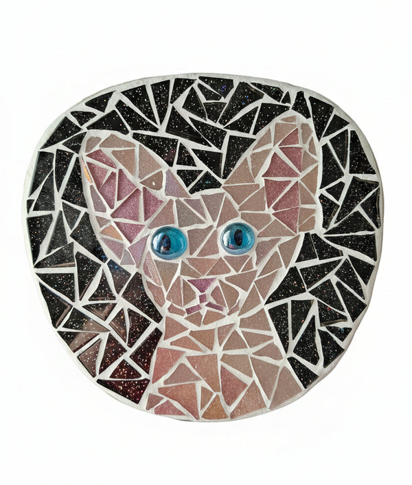 Circular mosaic wall art featuring a stylized cat design. Crafted with iridescent pink glass pieces on a sparkly black background, set on rustic wood.