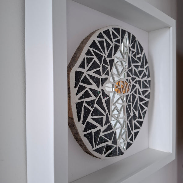 A circular mosaic wall art piece mounted inside a white frame. The design features a black and silver bat.