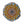 Circular mosaic wall art featuring a stylized sunflower design. Crafted with orange and yellow gold-dusted glass pieces on a pale blue background, set on rustic wood.