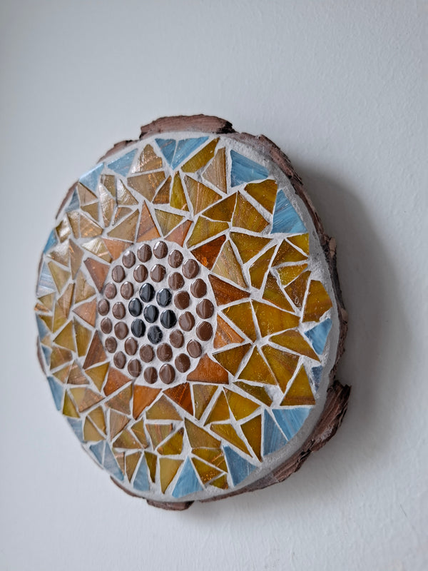 Side view of a circular sunflower mosaic artwork, showing the rustic wood edge.