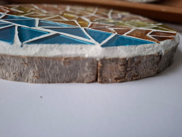 Side view of a circular sunrise mosaic artwork, showing the rustic wood edge.