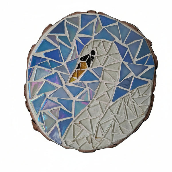 Circular mosaic wall art featuring a stylized swan design. Crafted with glittery white glass pieces on an iridescent blue background, set on rustic wood.