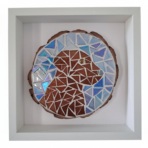 A circular mosaic wall art piece mounted inside a white square shadow box frame. The artwork features a brown dog surrounded by blue, light blue, and white geometric glass tiles.