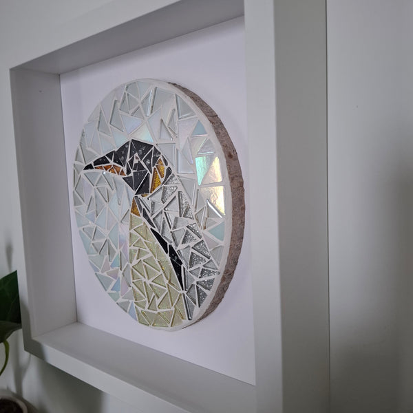 A circular mosaic wall art piece featuring a stylized penguin made of geometric glass tiles, mounted inside a white recessed wall frame.
