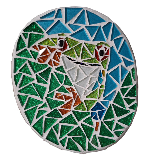 Circular mosaic wall art featuring a stylized tree frog design. Crafted with green, white and red glittery glass pieces on a glittery dark green background, set on rustic wood.