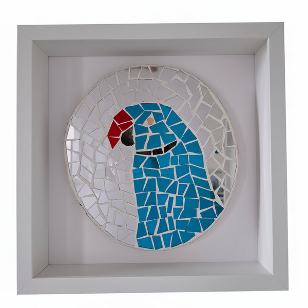 A square white shadow box frame containing a circular mosaic wall art piece of a parrot, featuring blue, red, black, and white glass tiles, displayed against a white wall.