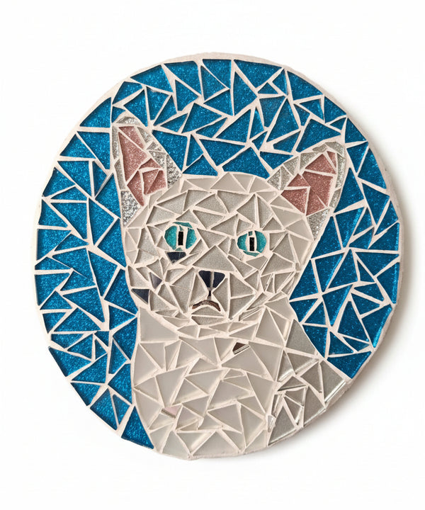 Circular mosaic wall art featuring a stylized cat design. Crafted with glittery white glass pieces on a sparkly blue background, set on rustic wood.
