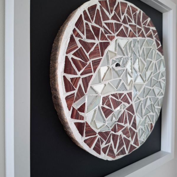 A circular mosaic wall art piece featuring an elephant, crafted with reddish-brown, white and mirrored silver pieces, mounted on a black background inside a white frame.