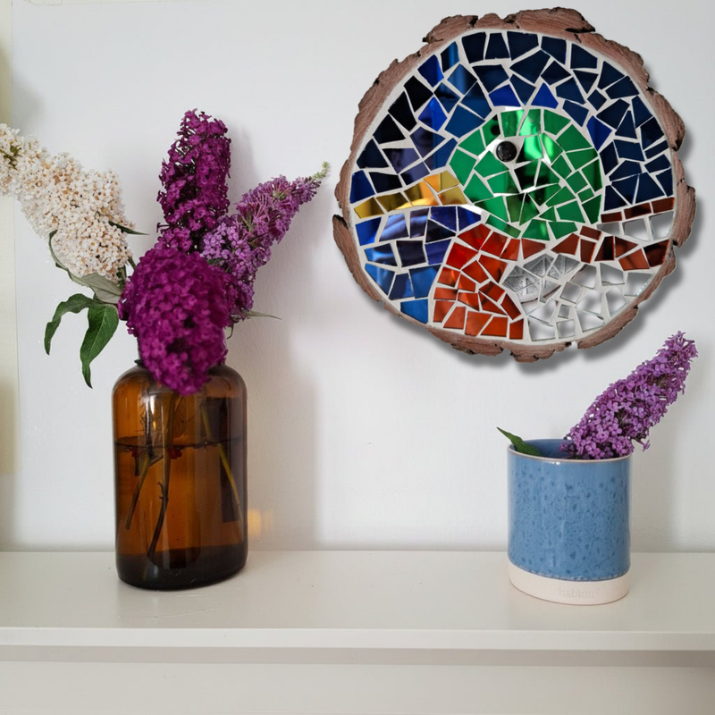 A decorative circular duck mosaic wall art piece with a natural wood edge hangs on a white wall above a shelf. The mosaic features blue, green, red, orange, and white tiles.