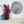 A round stained glass wall art piece featuring an elephant, displayed on a white wall above a shelf with purple and white flowers in vases.