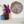 A round mosaic wall art piece featuring a stylized elephant face, displayed on a white wall above a shelf with decorative vases and flowers.