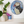 A circular mosaic wall art piece featuring a puffin in blue, black, white, and red, displayed on a white wall above a shelf with potted plants.