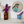 A circular mosaic wall art piece featuring a stylized bird in geometric segments, displayed on a white shelf next to two flower vases against a white wall.